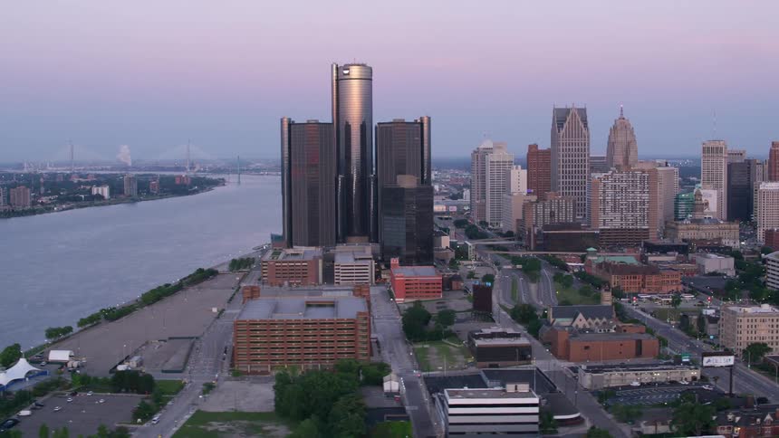 City skyline features skyscrapers and treelined streets at dusk with a river in the background
