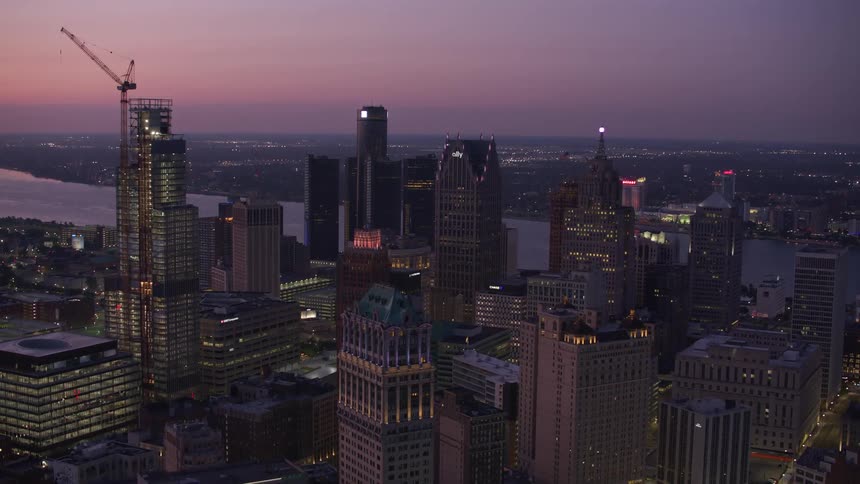 Aerial view of a city at dusk with illuminated skyscrapers and a river in the background