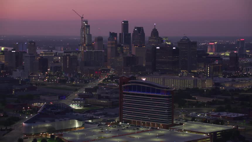 An aerial view of a metropolitan city at dusk with the lights of the buildings and streets on
