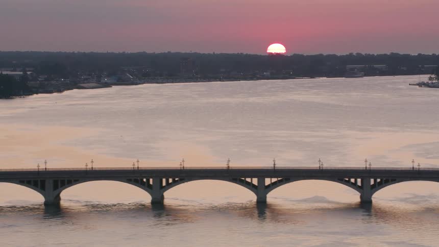 Aerial view of a long bridge spanning a sea channel and the sun setting on the horizon
