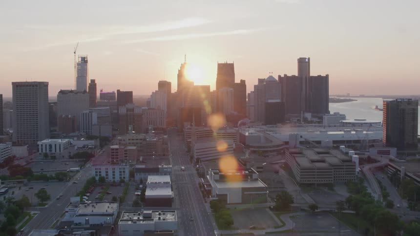 An aerial view shows the detroit skyline at sunset with the sun setting behind the city buildings