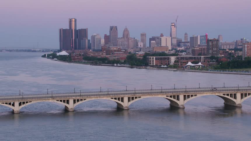 A bridge spans a wide river leading to a cityscape silhouetted against a twilight sky