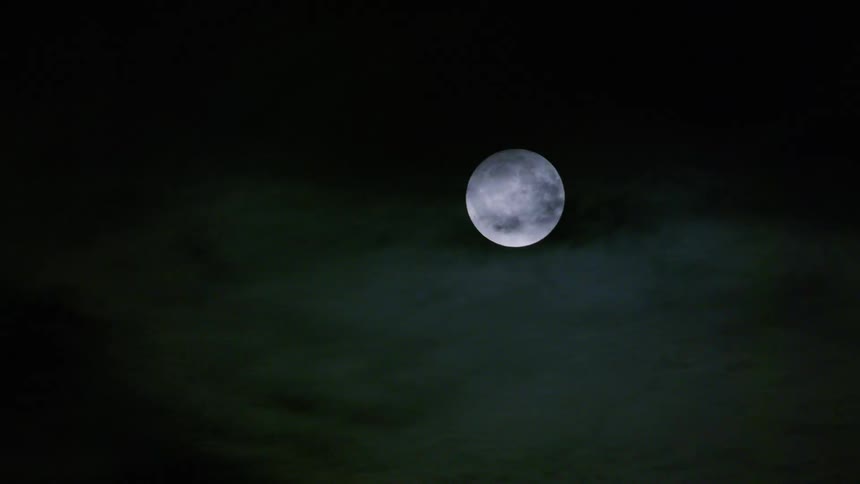 A full moon glows against a dark night sky partially obscured by wisps of clouds