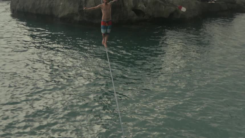 A man balances on a rope over a rippling body of water