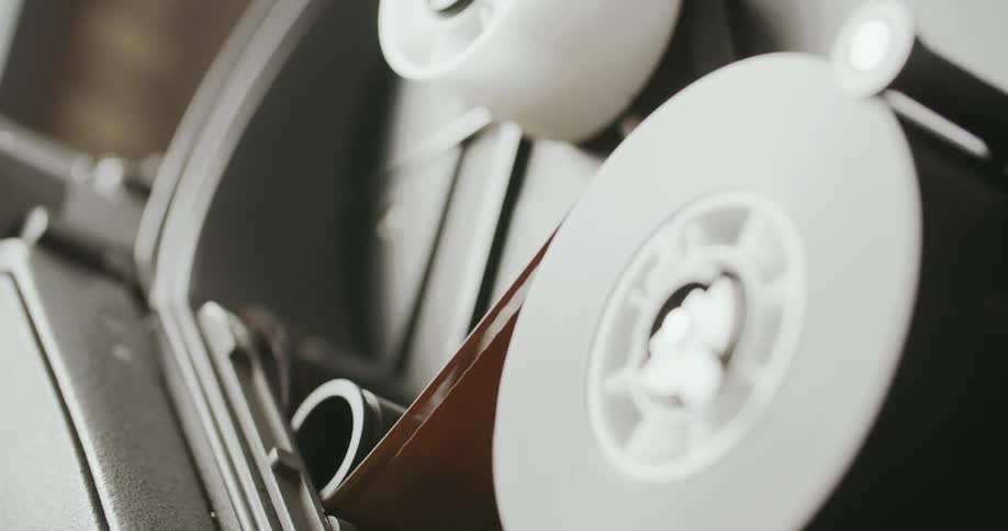 A vintage projector whirs softly as it pulls film tape through its reels continuing until the tape ends and the machine stops capturing a moment of cinematic nostalgia