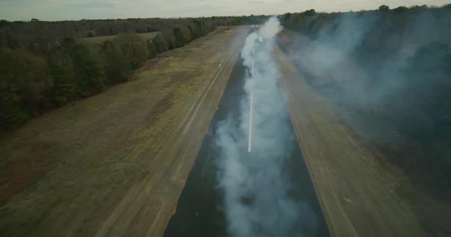 A plane is flying low tot he road leaving a huge trail of smoke