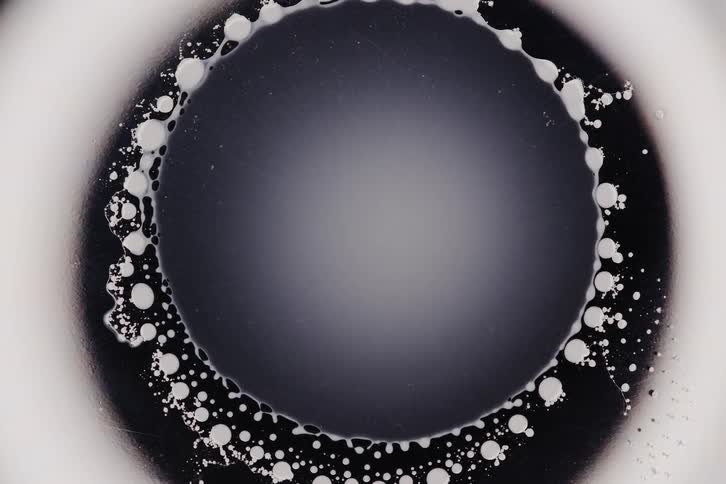 A dark circular center contract inwards surrounded by a ring of white droplets and a darker outer edge creating a dynamic abstract pattern