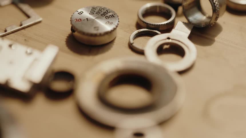 Small disassembled metal parts including rings and a numbered dial are scattered on a wooden surface