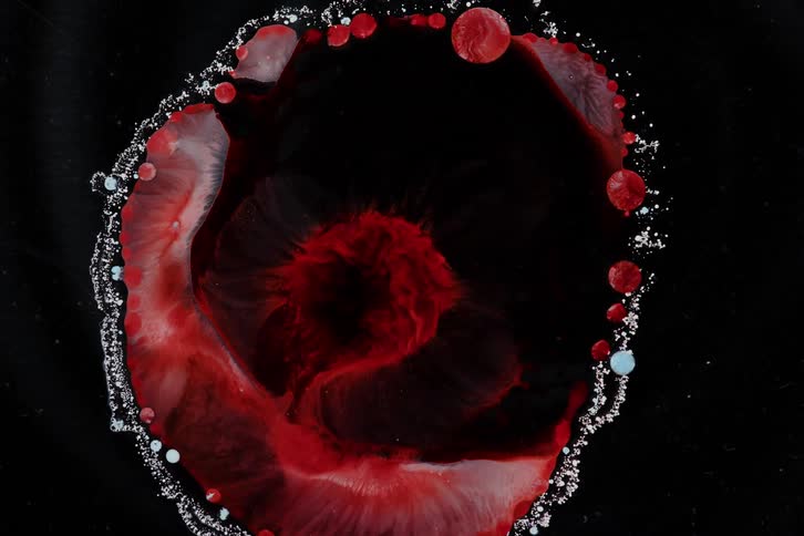 Extreme close up of a liquid of organic matter expanding with molecules against a black background