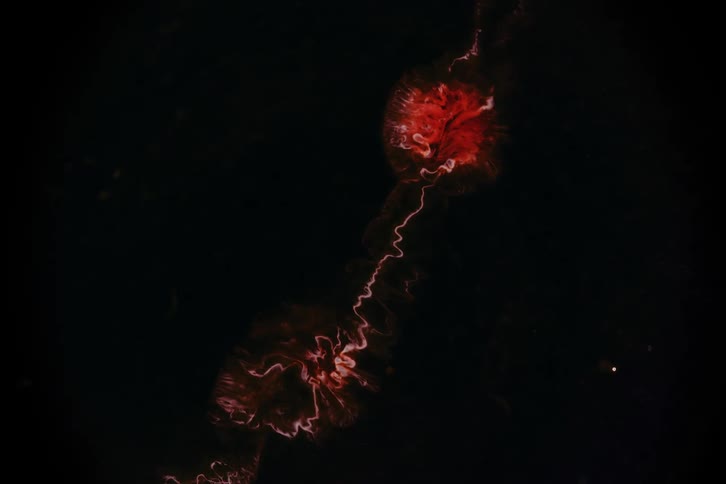 An aerial view captures fiery red shapes swirling and expanding in a dark expanse forming a hypnotic lavalike display that intensifies as the camera descends