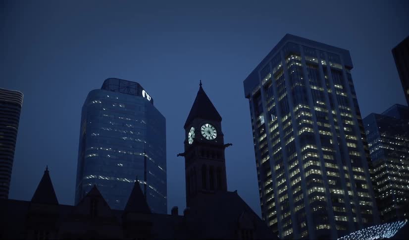 Illuminated clock tower at night surrounded by buildings of a metropolis