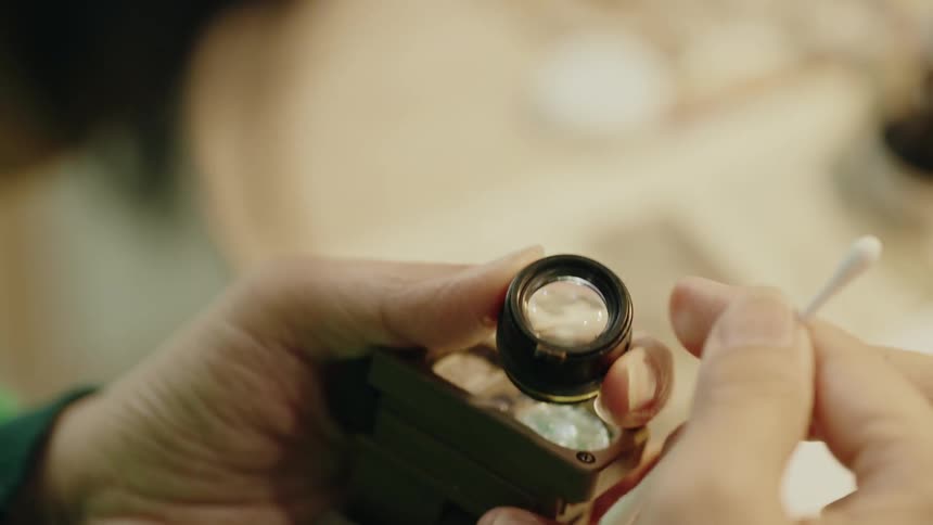 A technician carefully cleans the lens of a disassembled vintage camera in a workshop