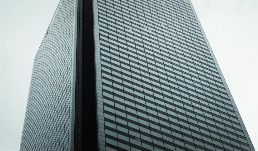 A lowangle shot shows a tall skyscraper with a gridlike facade of alternating dark and light panels against a cloudy sky