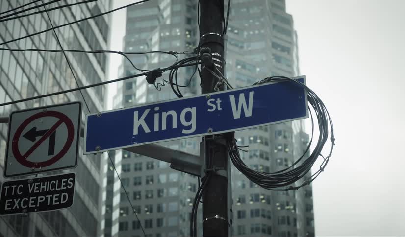 A street sign reading king st w is attached to a pole with overhead wires next to traffic sign below and a tall building in the background