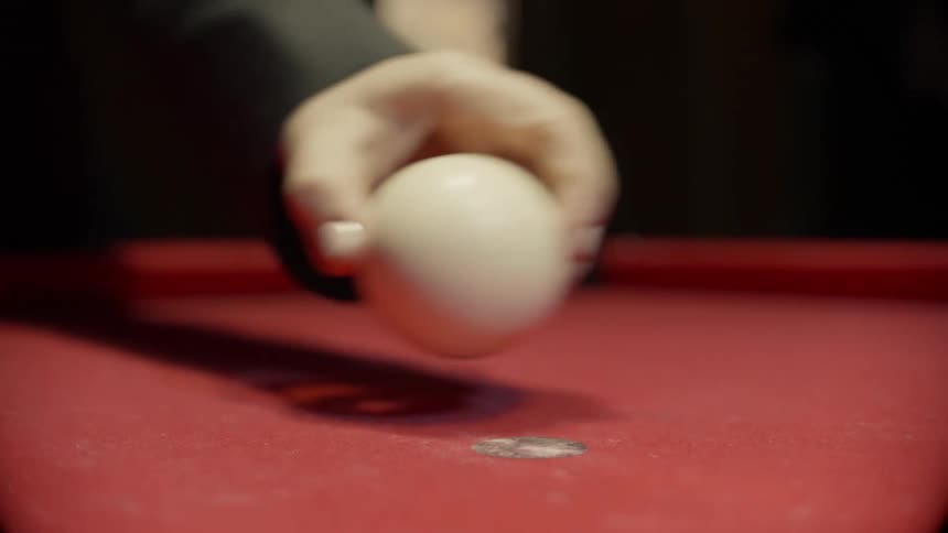 A man places the cue ball on the pool table
