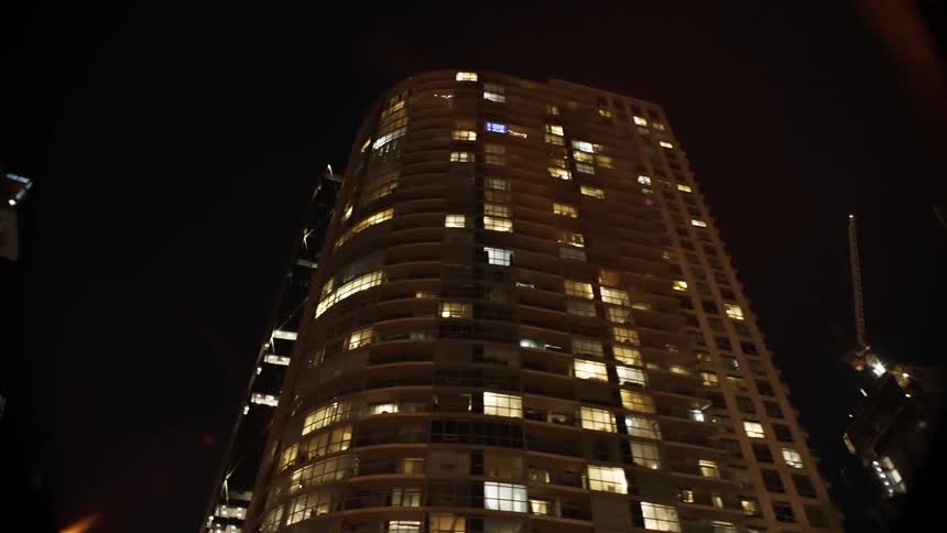 A night cityscape showing tall buildings with lit windows and a bright beam of light ending with a streetlamp in the foreground