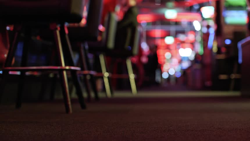 In a vibrant casino a pig with a bell collar dashes down a corridor past gambling machinesblinking lights emphasizing the energetic casino atmosphere with a seated person at the bar counter and bar stools further in the background