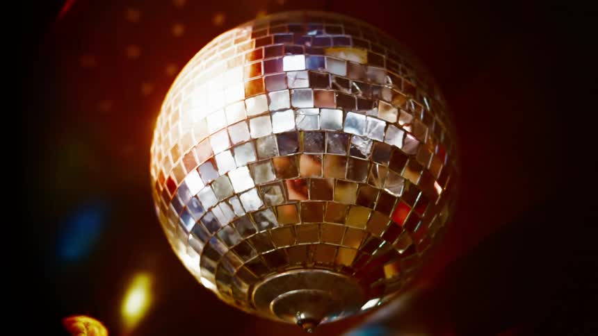 Shiny disco ball with lights spinning from ceiling in a dark room