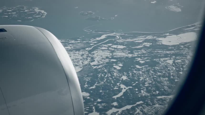 View from an airplane window of an airplane engine and the frozen land and the ocean below