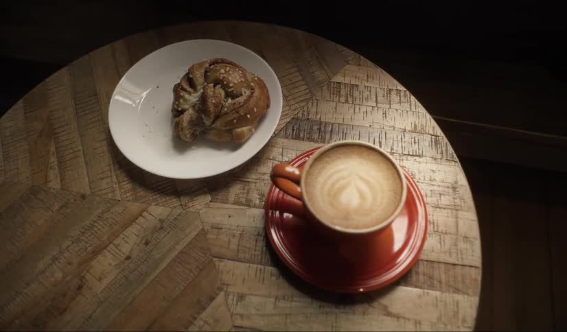 Latte in red coffe cup and pastry on white plate sitting on round wood table