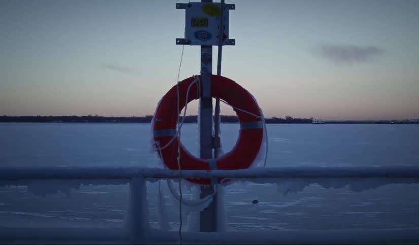 Orange lifebuoy is attached to a pole on an icecovered pier with a frozen lake in the background