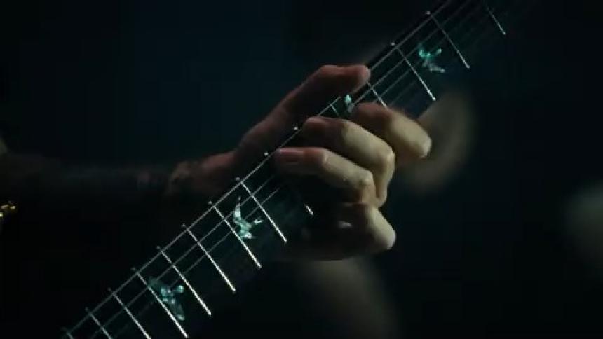 Male guitarist with a tattooed arm plays the guitar during a performance