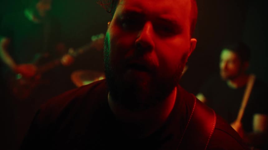 Portrait of a vibrant man singing and two others behind playing guitar and drums in a performance