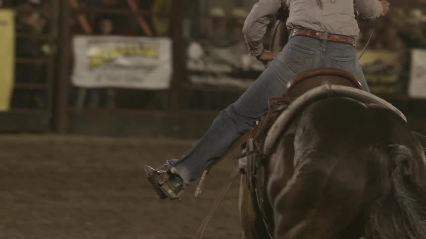 Competitor riding a horse participates in a rodeo event in front of an audience