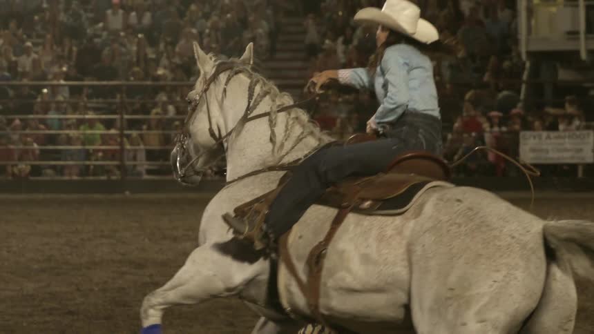 Rider leads a white horse at high speed around a barrel during a rodeo competition