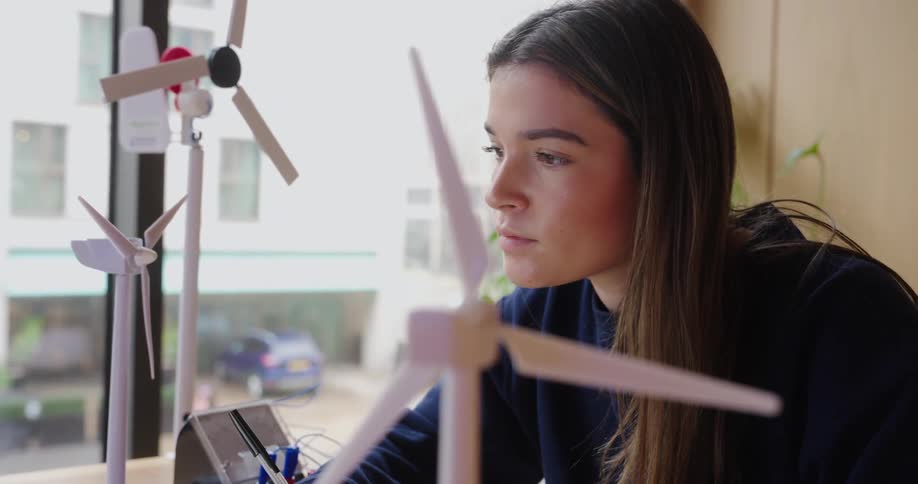Woman looks closely at a model wind turbine while working in a bright environment