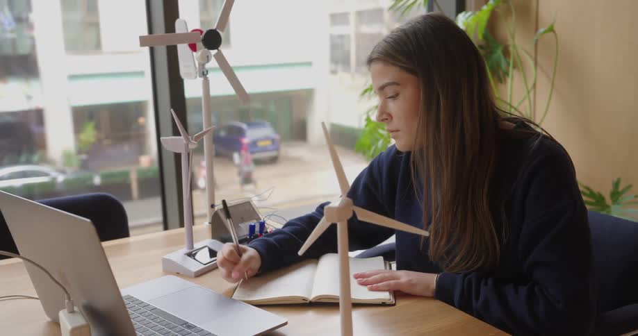 Woman writing in a notebook and analyzing a wind turbine