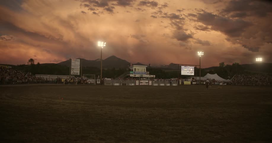 Crowd of people in the stands at an openair rodeo in the late afternoon