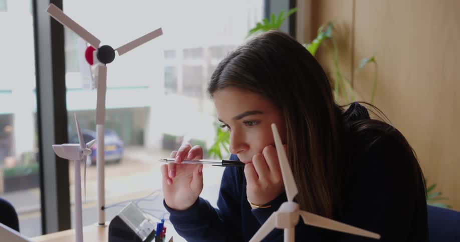 Young woman works intently on her laptop surrounded by models of wind turbines on the table