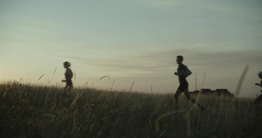 Group of people run through an open field at dusk