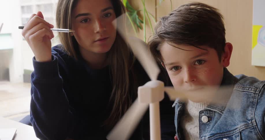 Young woman and a boy watch intently as a model of a wind turbine rotates on a table