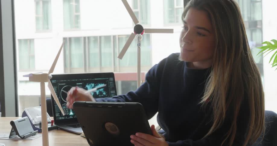 Woman holding a tablet and taking notes in a notebook while interacting with miniature wind power prototypes