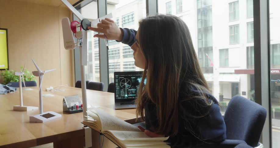 Young woman holding a notebook and analyzing prototype of a wind energy model