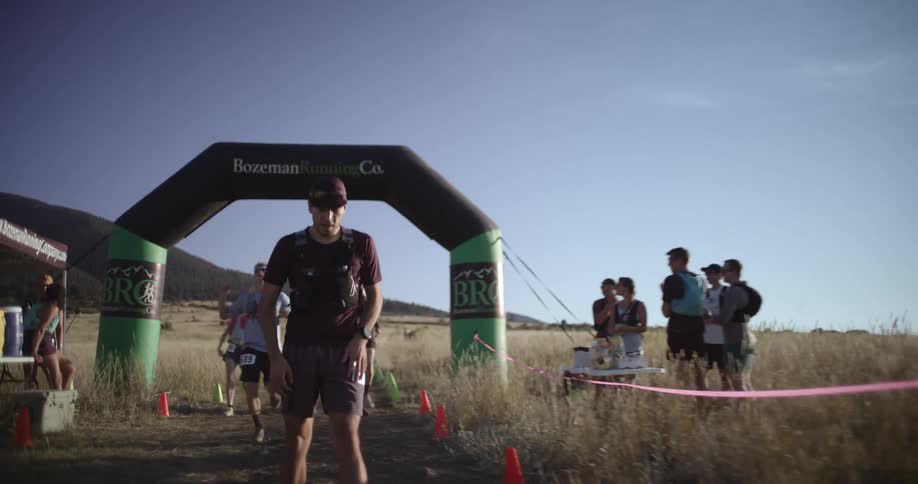 Man crossing the finish line of an outdoor race with inflatable arch and spectators in the background