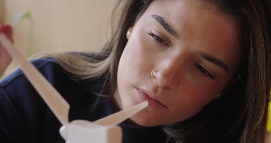The face of a young woman who is looking at an object with white rods in front of her and spinning one of them