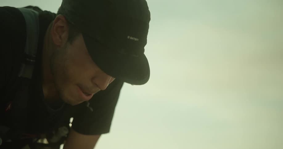 Sweaty exhausted runner leans forward wearing a black cap as he catches his breath