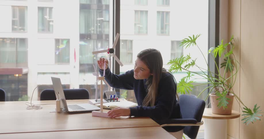 A girl is sitting in the office examining a model of a windmill