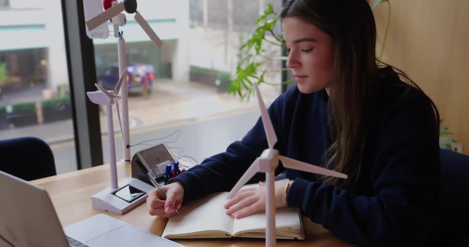 Young woman writing in a notebook in front of a laptop