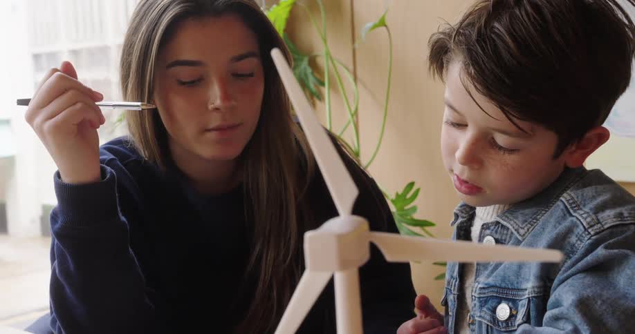 Woman and a boy look closely at a model wind turbine while discussing something
