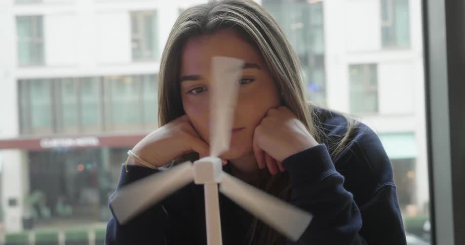 The face of a young woman spinning a white threepropeller device and looking at it