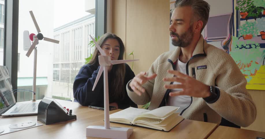 Man explaining about wind energy platform with prototype in front of him to young woman