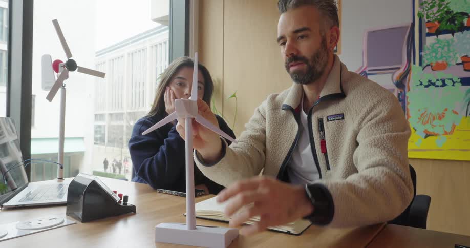 Man in an office environment teaching a young woman and interacting with an abstract wind energy platform