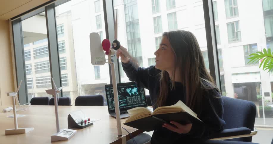 A woman examines a wind turbine model while holding a notebook in a meeting room