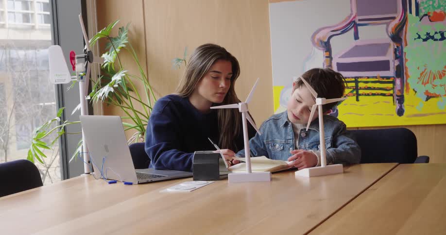 Young woman next to a child who is reading a book at a table