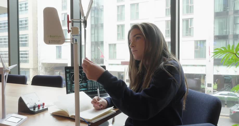 A teenager is writing notes while looking at a model of a windmill