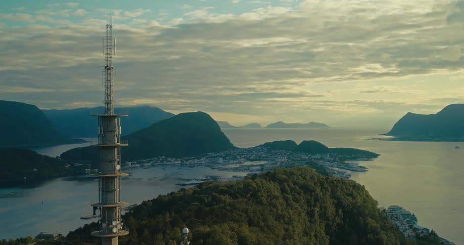 Telecommunications tower stands out over a mountainous landscape with islands and calm waters at dusk